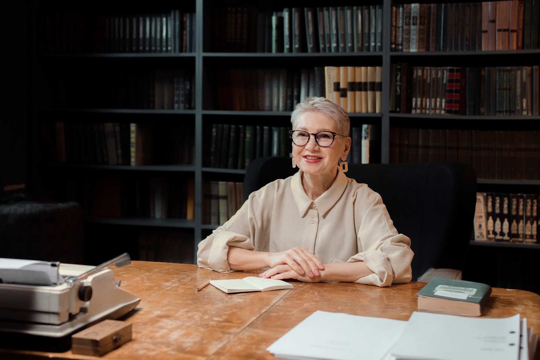 Writer at a wooden desk with open notebooks and scattered papers