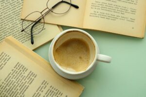 A person reading an open book beside a coffee cup at a wooden table
