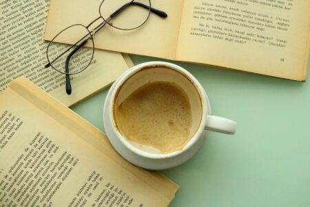 A person reading an open book beside a coffee cup at a wooden table