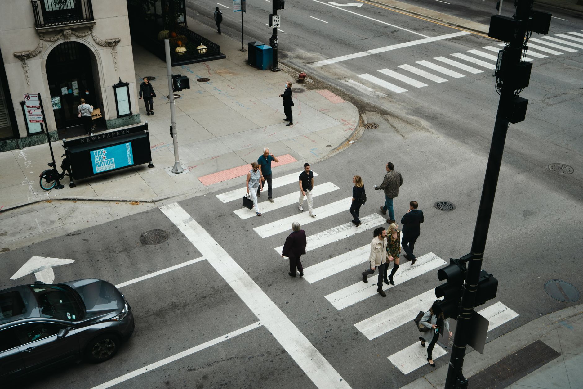 People walking along a busy city sidewalk past storefronts in a dense urban neighborhood
