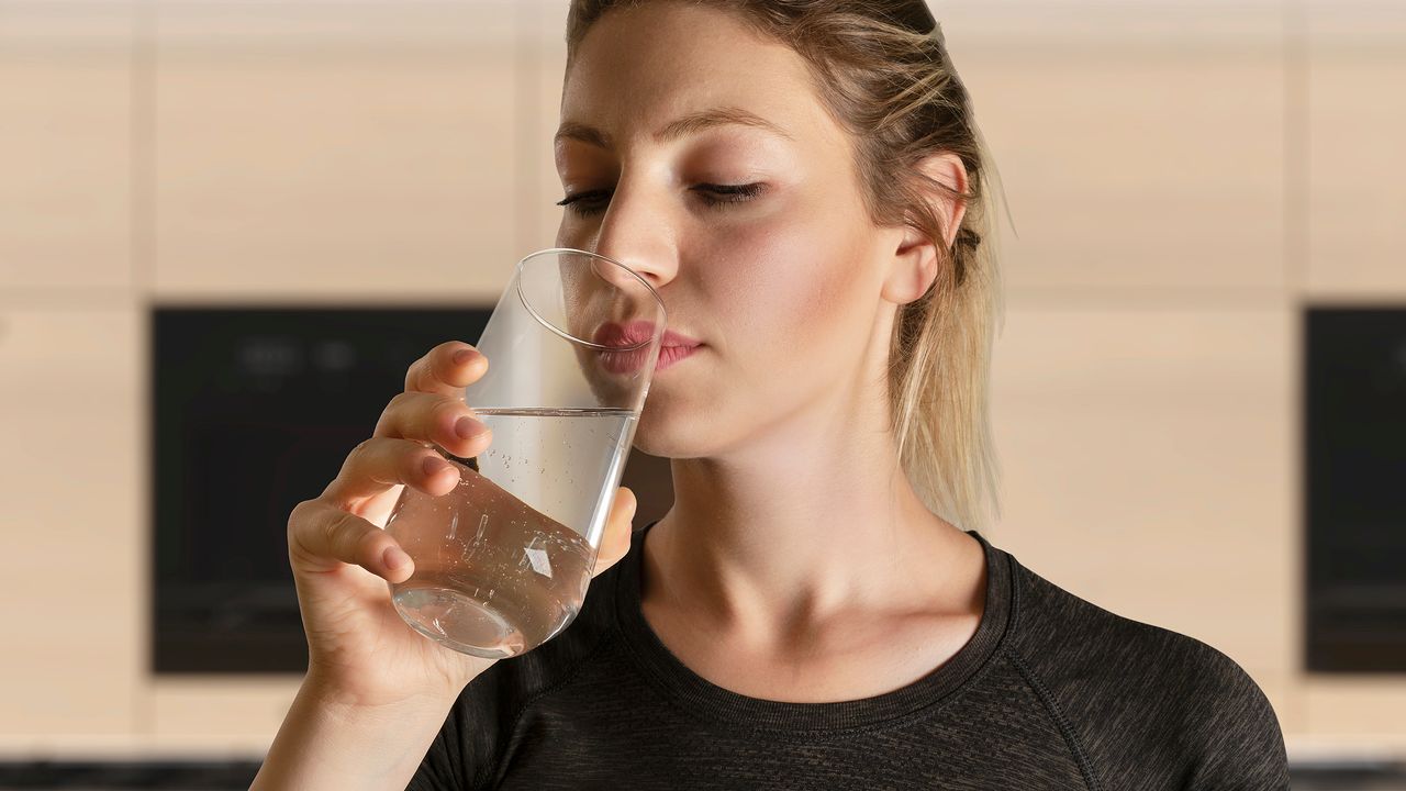 A woman sitting at a table reading a handwritten note with a glass of water nearby