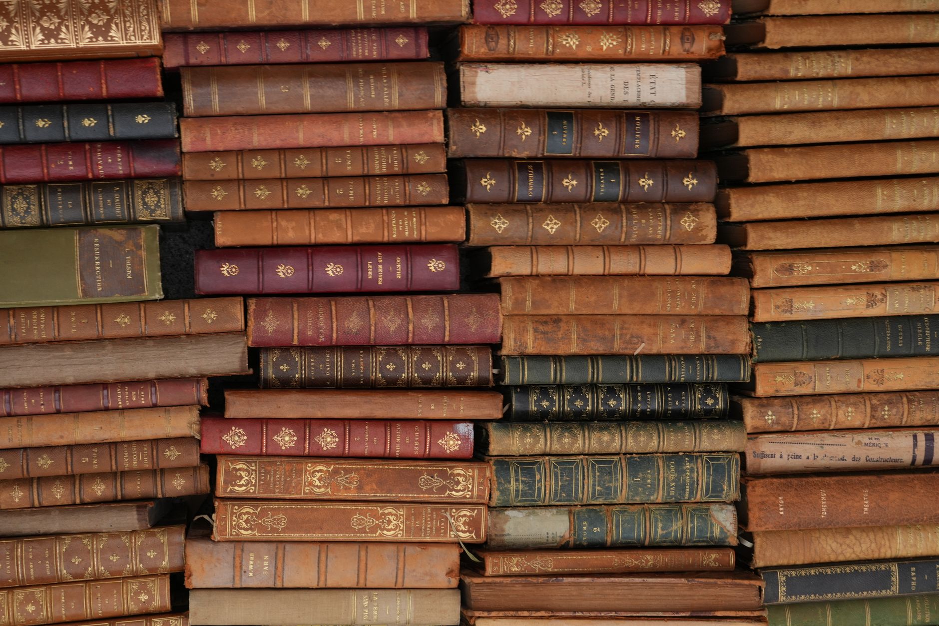 Stacked antique books on a wooden shelf in a dim library