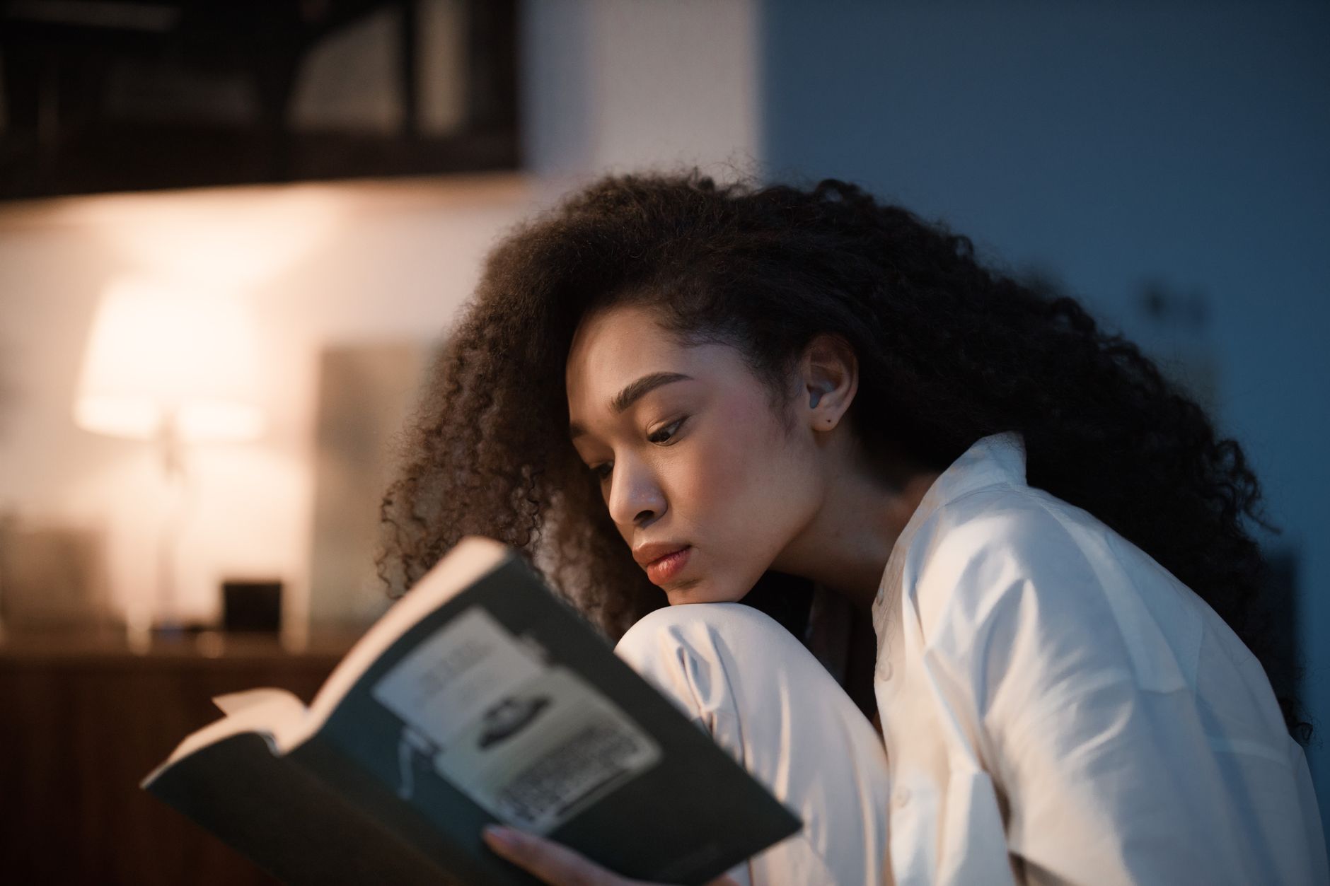 A person reading a book alone at a table in low light