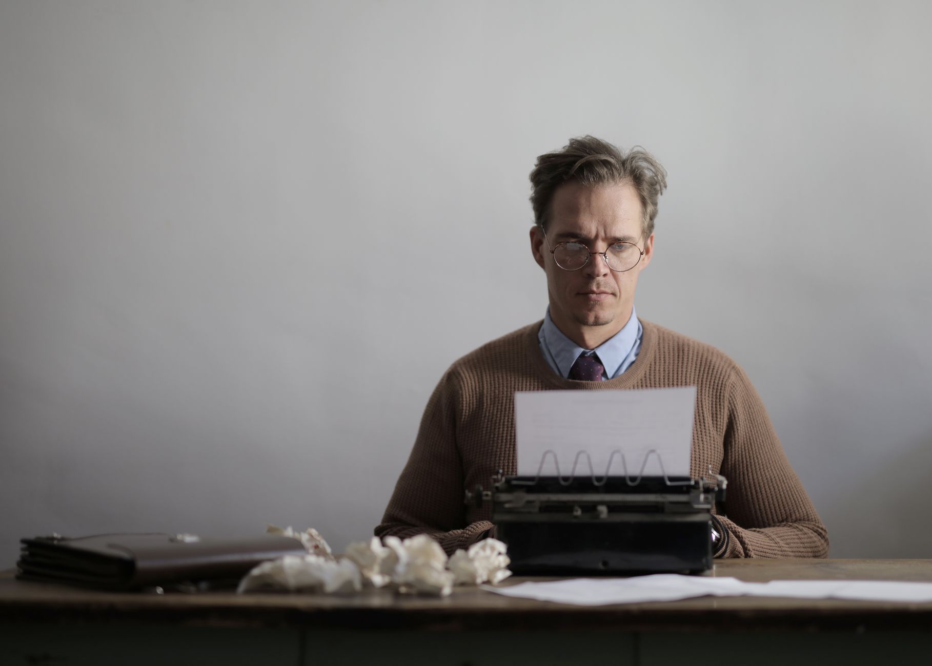Writer working at a desk with a laptop and scattered manuscript pages