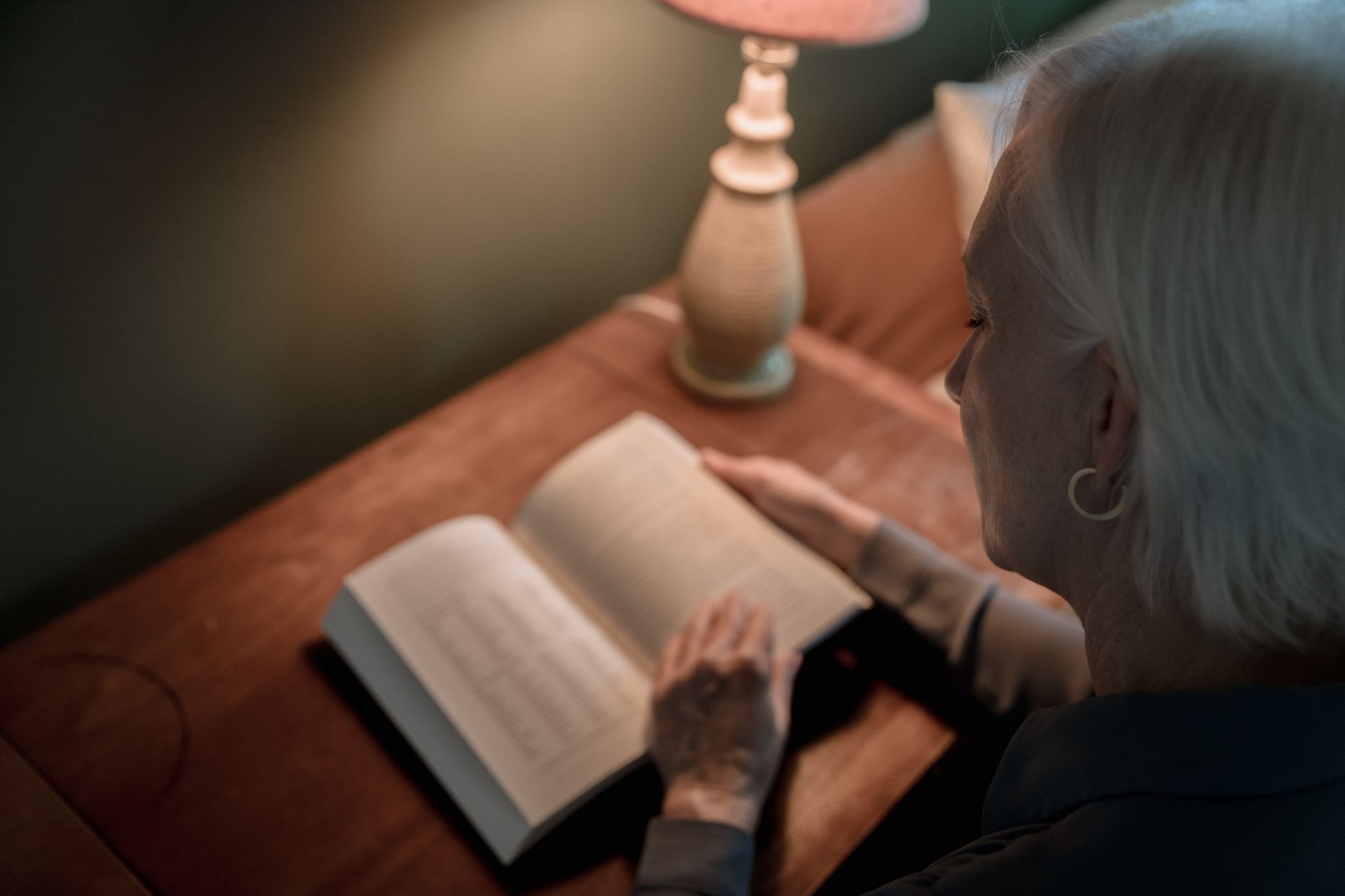 Person reading a book alone under a single lamp in a dark room