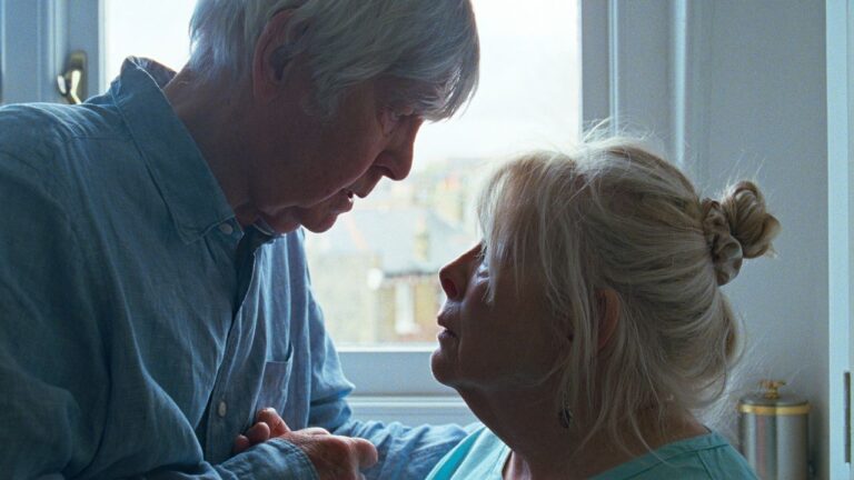 An elderly woman sitting by a window, light falling across her face, looking away from the camera