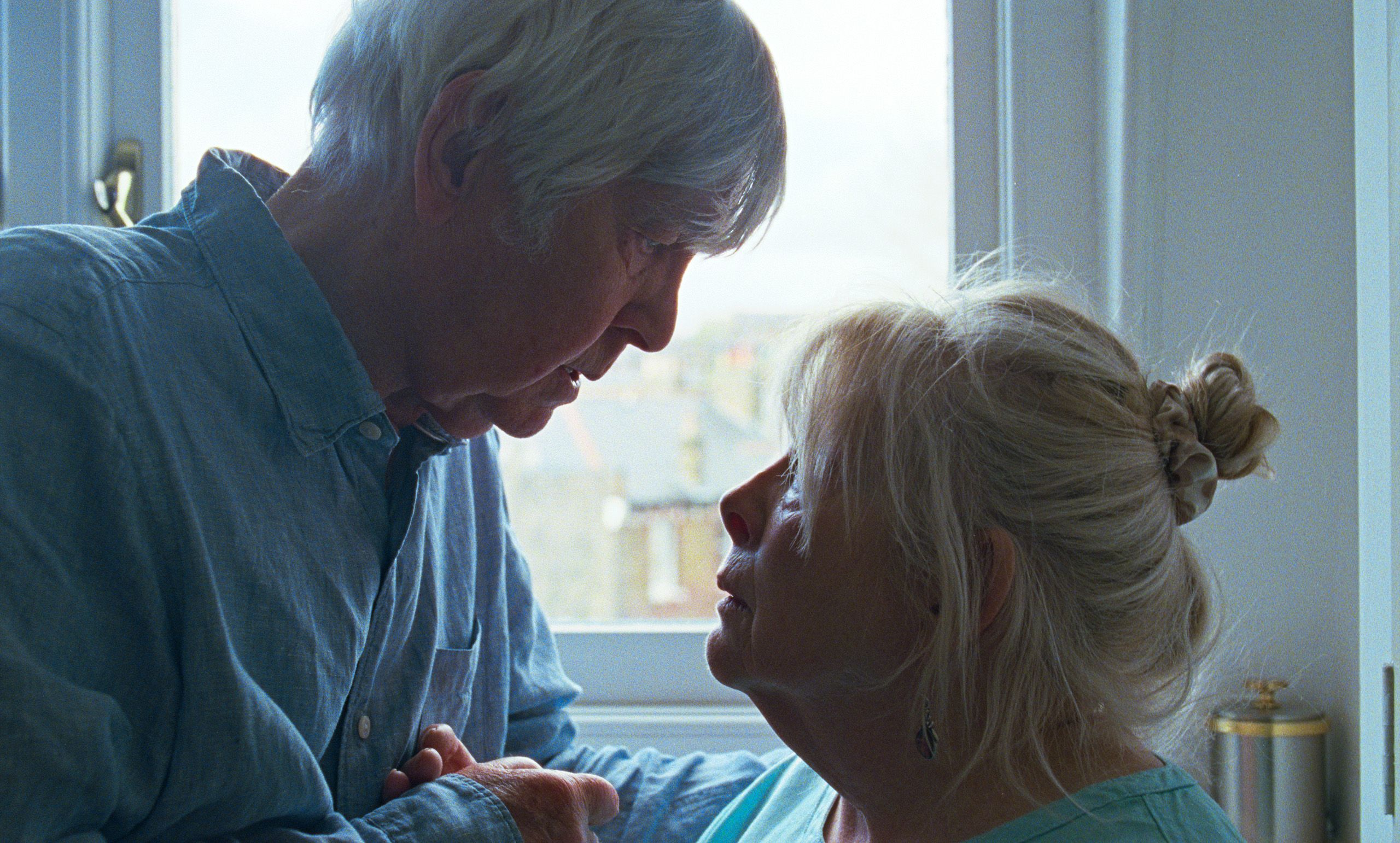 A caregiver sitting beside an older person in a quiet domestic interior